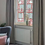 MainZauber Apartments früher MainTerrasse Miltenberg am Main - Gemütliche Luxus-Ferienwohnung AltstadtZauber Miltenberg: graue Vorhänge, Blick auf Fachwerk, Blumen, inspirierendes Zitat.