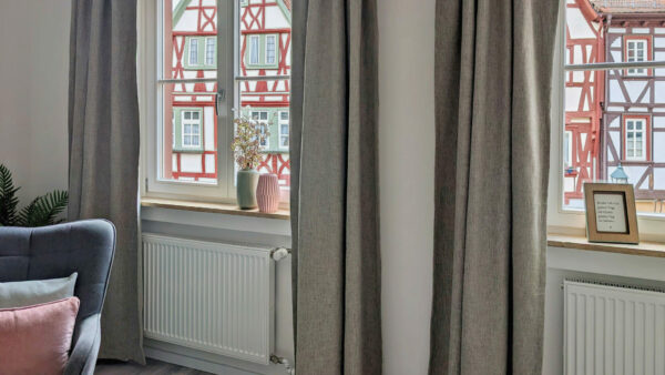 MainZauber Apartments früher MainTerrasse Miltenberg am Main - Gemütliche Luxus-Ferienwohnung AltstadtZauber Miltenberg: graue Vorhänge, Blick auf Fachwerk, Blumen, inspirierendes Zitat.