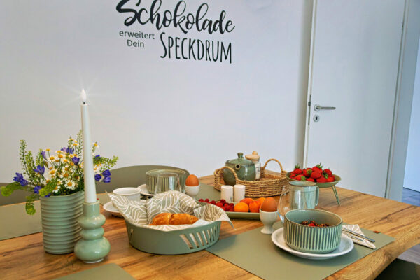 MainZauber Apartments früher MainTerrasse Miltenberg am Main - Luxuriöses Frühstück in stilvoller Ferienwohnung: Grünes Geschirr, Croissants, Obst & Deko im Altstadt-Apartment.