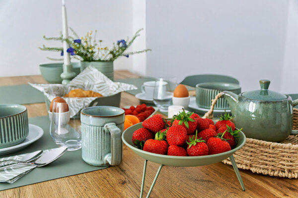 MainZauber Apartments früher MainTerrasse Miltenberg am Main - Frühstückstisch im Luxus-Apartment AltstadtZauber Miltenberg mit grünem Geschirr, Croissants, Obst - perfekte Unterkunft.