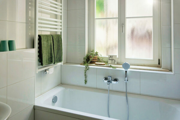 MainZauber Apartments früher MainTerrasse Miltenberg am Main - Modernes, weiß gefliestes Badezimmer in der Luxus-Ferienwohnung AltstadtZauber Miltenberg mit Badewanne, Fenster, Handtüchern.