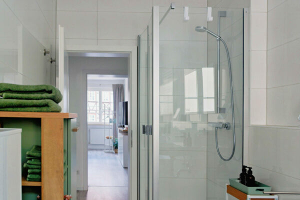 MainZauber Apartments früher MainTerrasse Miltenberg am Main - Modernes Bad in Luxus Ferienwohnung mit Glasdusche, Holzbord, grünen Handtüchern und Blick ins helle Wohnzimmer der Unterkunft.