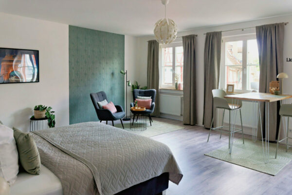 MainZauber Apartments früher MainTerrasse Miltenberg am Main - Luxuriöse Ferienwohnung in der Altstadt: Modernes Studio, großes Fenster, stilvolle Sitzgruppe, Esstisch & gemütliches Bett.