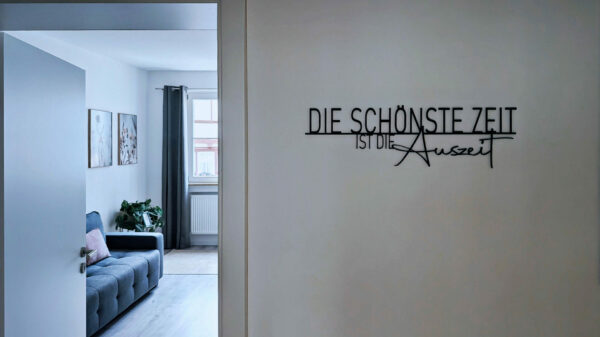 MainZauber Apartments früher MainTerrasse Miltenberg am Main - Modernes, minimalistisches Wohnzimmer in einer Luxus-Ferienwohnung: graues Sofa, Kunst, Fenster, Spruch 
