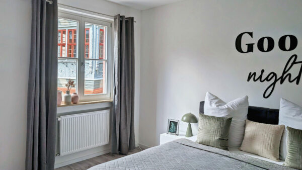 MainZauber Apartments früher MainTerrasse Miltenberg am Main - Helles Schlafzimmer in Luxus-Ferienwohnung mit gemütlichem Bett, Dekokissen, grüner Lampe, Blick auf Altstadt Miltenberg.