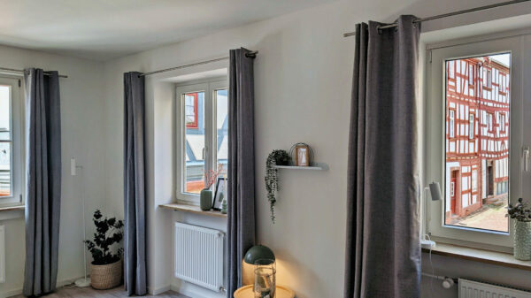 MainZauber Apartments früher MainTerrasse Miltenberg am Main - Helle Luxus-Ferienwohnung mit weißen Wänden, drei Fenstern, Top-Ausstattung und Blick auf Fachwerkhäuser in Miltenberg.