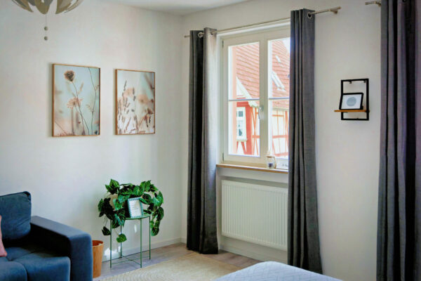 MainZauber Apartments früher MainTerrasse Miltenberg am Main - Helles Wohnzimmer im Luxusapartment AltstadtZauber Miltenberg: Pflanzenkunst, Navy-Sofa, großes Fenster, perfekte Ferienunterkunft.