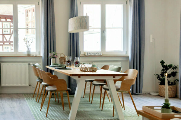 MainZauber Apartments früher MainTerrasse Miltenberg am Main - Luxuriöse Ferienwohnung in Altstadt: Moderner Essbereich für 6 Personen, helle Fenster, Holzmöbel, grüner Teppich, gemütliche Atmosphäre.