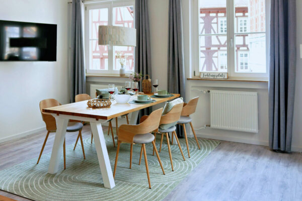 MainZauber Apartments früher MainTerrasse Miltenberg am Main - Luxuriöses Esszimmer der Ferienwohnung AltstadtZauber Miltenberg: großer Holztisch, helle Stühle, moderne Ausstattung, viel Licht.