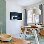 MainZauber Apartments früher MainTerrasse Miltenberg am Main - Luxuriöse Ferienwohnung in Miltenberg: Moderner Wohn-Essbereich mit Holztisch, TV, Kerze und stilvoller Akzentwand.