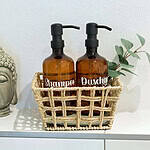 MainZauber Apartments früher MainTerrasse Miltenberg am Main - Zwei bernsteinfarbene Spender für Shampoo und Duschgel im Korb, neben Buddha und Eukalyptus - Luxus-Apartment Flair.