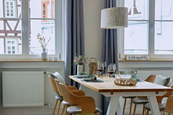 MainZauber Apartments früher MainTerrasse Miltenberg am Main - Helle Ferienwohnung mit luxuriösem Essbereich, Holztisch für 4, blauen Vorhängen und moderner Unterkunftsausstattung.