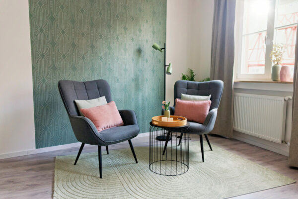 MainZauber Apartments früher MainTerrasse Miltenberg am Main - Helles Luxus-Apartment: Zwei moderne graue Sessel mit pinken Kissen, runder Couchtisch, großes Fenster, stilvolle Unterkunft.