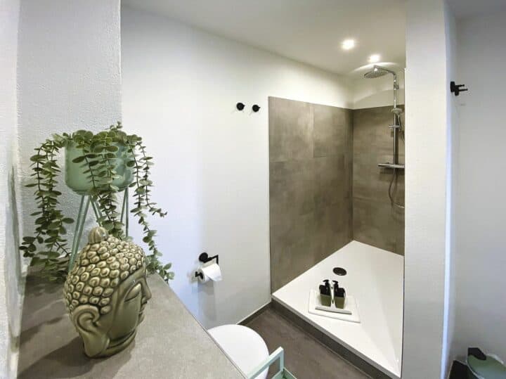 MainZauber Apartments früher MainTerrasse Miltenberg am Main - Entdecken Sie das perfekte Urlaubserlebnis in der Ferienwohnung Miltenberg, wo Luxus auf modernes Design trifft. Diese exquisite Unterkunft verfügt über ein elegantes Badezimmer mit ebenerdiger Dusche im Betonstil und luxuriösen Toilettenartikeln. Genießen Sie die beruhigende Note einer Topfpflanze und einer Buddhakopf-Dekoration, die zur Atmosphäre beitragen. Die minimalistischen Akzente, darunter makellos weiße Wände und elegante Einbauleuchten, schaffen eine beruhigende MainTraum-Atmosphäre für Ihren unvergesslichen Aufenthalt.